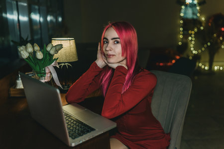 The red-haired woman in a red dress sits and uses the laptop.の写真素材