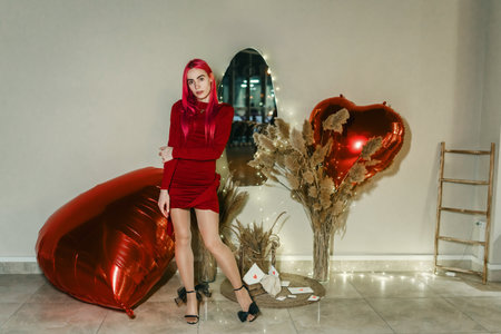 Sexy woman with red hair and red dress poses among inflatable heartsの写真素材