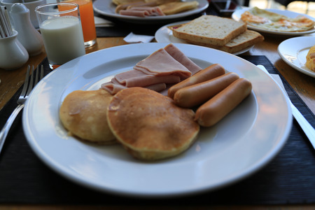 Breakfast of buttermilk pancakes with sausages, ham, toasts, milk and orange juiceの写真素材