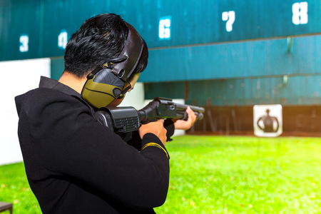 A woman soldier with law enforcement aim a long shotgun to target in martial arts for self defense in an emergency case. Shooting gun by two hand in academy shooting range.の写真素材