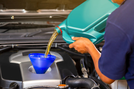 Car mechanic replacing and pouring fresh oil into engine at maintenance repair service station
