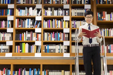 The professor librarian standing on stairs for searching knowledge, reading book in the library.