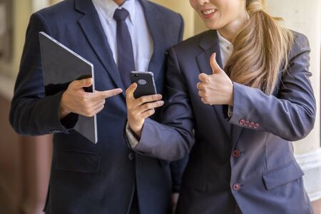 Two business people standing in office , looking at smart mobile phone.の写真素材