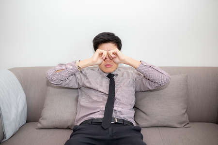 Tired young man massaging eyes in front of laptop. Eyes fatigue, headache or migraine at workplace.の写真素材