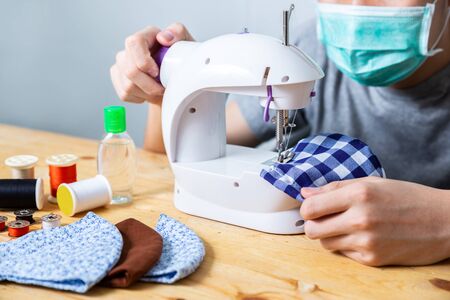 Woman sewing cloth cotton face mask to protect against the virus at home. Homemade handicraft protective mask against covid 19 virus. Reusable face mask.の写真素材