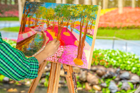 The artist paints and sketch a picture outdoors in the early sunny morning. Painting in nature.
