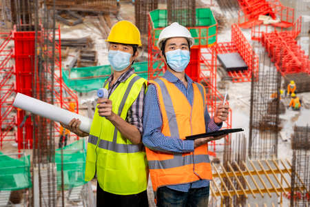 Two young asian engineers wearing surgical mask with tablet and blueprint New normal concept. (With...