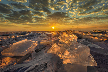 Sunset reflected in a large block of ice hummock on the frozen lake background.