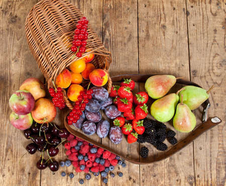 Freshly harvested seasonal Fruits, with a Basket on a wooden Tableの写真素材
