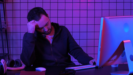 Tired hacker sleeping near computer while computer processing.の写真素材