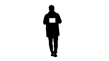 Silhouette Young man walking, talking and showing digital tablet with white screen mockup.の写真素材