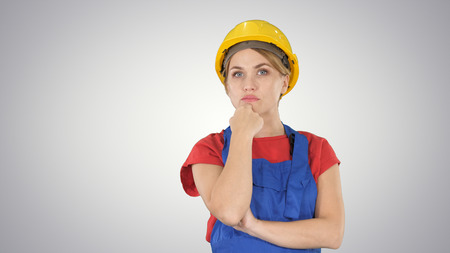Thinking construction worker woman wearing builder helmet on gradient background.の写真素材