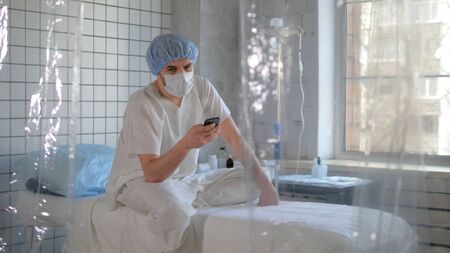 Isolated person in madical mask using his phone in a hospital.の写真素材