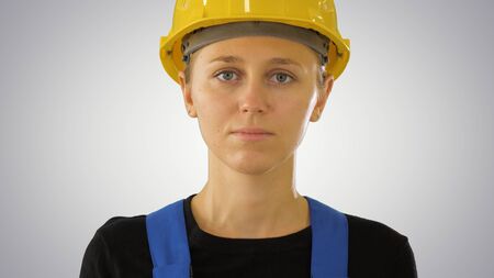 Young attractive caucasian woman builder in the hard yellow helmet on gradient background.