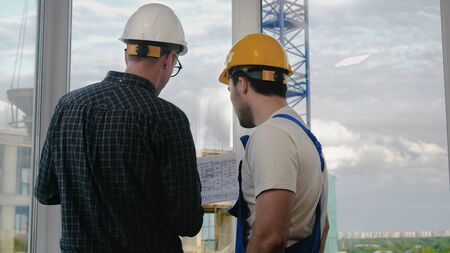 Medium shot. Back view.Engineer and worker looking at blueprint. Professional shot  025. 