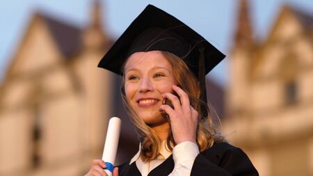 Happy pretty girl graduate in gown talking on mobile phone.の写真素材