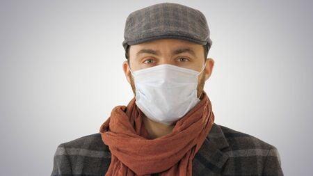 Handsome young European man in trendy coat wearing disposable protective face mask on gradient background.の写真素材