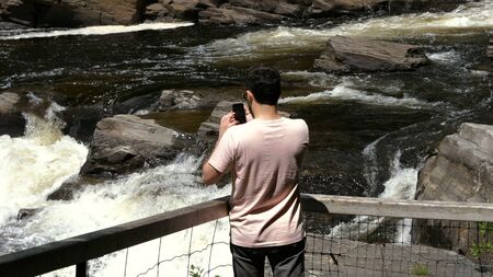 Medium shot.Man taking a picture of a waterfall on smartphone. Travel concept. Professional shot  02. の写真素材