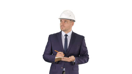 Engineer in suit and helmet walking and writing notes in notepad on white background.の写真素材
