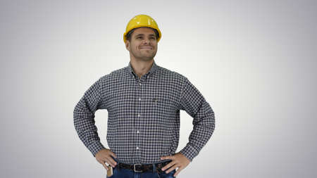 Smiling construction worker in yellow helmet looking at perfect well built object Hands on hips on gradient background.の写真素材