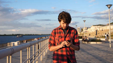 Casual man walking outdoors reading text message on his smart phone.