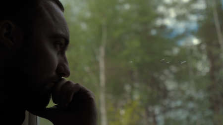 Man looking out window with chin on hand in a train, serious expression.