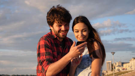 Happy couple watching photos in a smart phone outdoors.