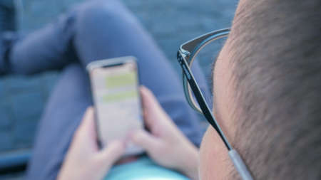 Man using his smartphone writing a message sitting on a bench.の写真素材