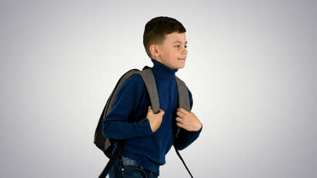 Cheerful boy in polo neck walking with a backpack on gradient ba