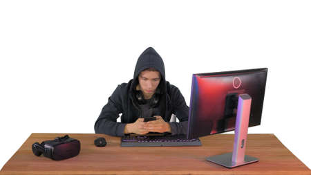 Hooded hacker using laptop and smartphone on white background.の写真素材