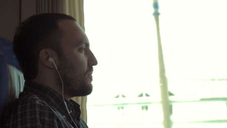 A Man listening to the music with earbuds from a smart phone in a train.