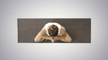 Woman folding legs in to lotus pose on gradient background.