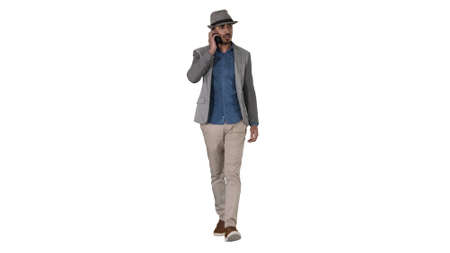 Happy young North African man talking on mobile phone while walking on white background.の写真素材