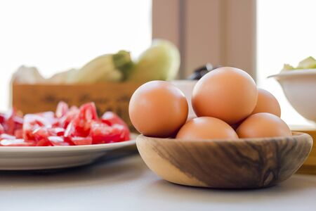 Plates with sliced vegetables and eggs with olives in bowls on kitchen table, cooking process...