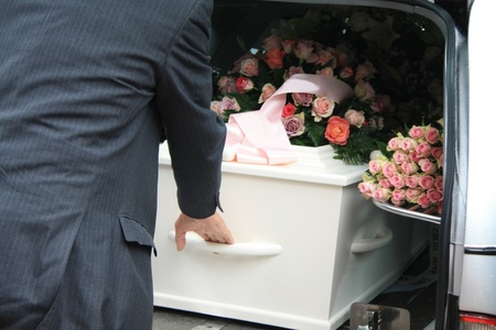 A funeral home employee takes out a white coffin of a hearseの写真素材