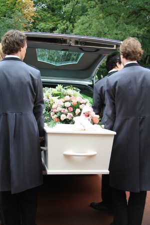 Funeral home employees take out a white casket of a hearse