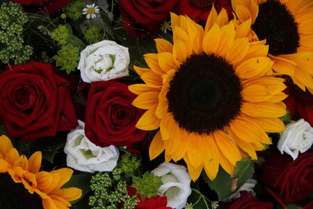 Bright yellow sunflowers and big red roses in a floral arrangementの写真素材