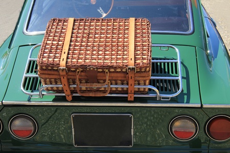 Classic wicker suitcase on back side of an old car