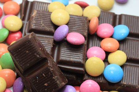 Chocolate filled candies in various bright colors and pieces of a chocolate barの写真素材