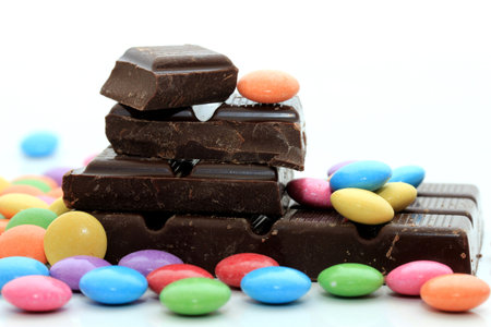 Chocolate filled candies in various bright colors and pieces of a chocolate barの写真素材