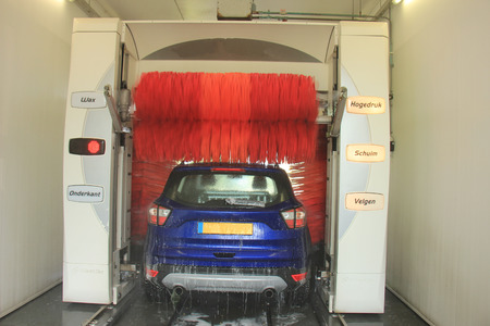 A blue SUV in an automatic car wash. Text on machine: program items in Dutch.の写真素材