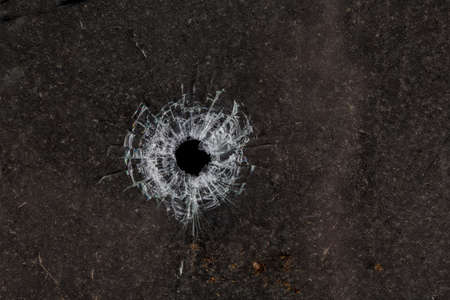 Bullet hole in glass on dirty grungy black backgroundの写真素材