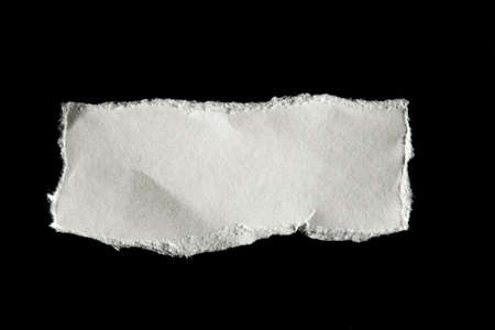 Piece of torn paper on black with rough edges.の写真素材