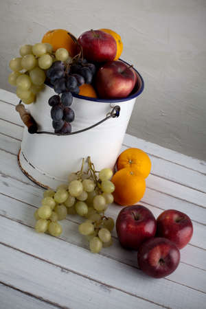 a fruit still life composition with grapes, apples, and oranges in a very old metal bucketの写真素材