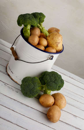potatoes and broccoli in an old iron bucket on a wood tableの写真素材