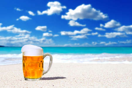 Beer in a glass mug on a white sand beach backgroundの写真素材