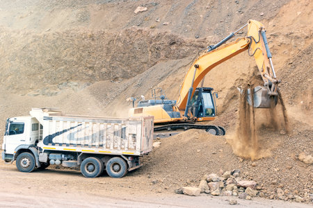Excavator loading sand into dump truck at a construction site.の写真素材