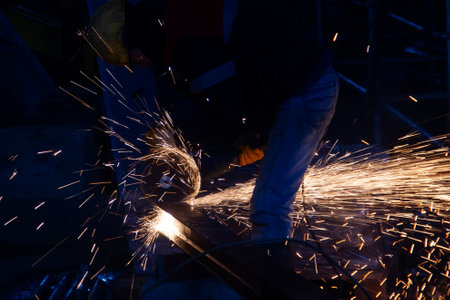 Industrial worker cutting metal with angle grinder in a factory. The worker is cutting a steel material with a grinding machine in the construction site.の写真素材