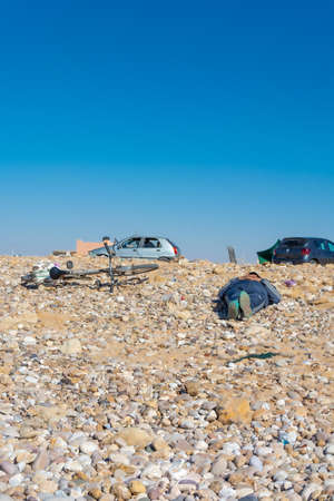 Laayoune port, Morocco, Western Sahara - January 6, 2019: a dressed man with a bicycle lies on the stones and sunbathes on the beach under a blue sky. Copy space. Verticalのeditorial素材
