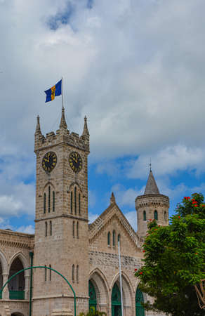 Bridgetown, Barbados, Caribbean - 22 Sept 2018: Parliament building with flag and clock tower. White clouds in the blue sky. Copy space. Verticalのeditorial素材